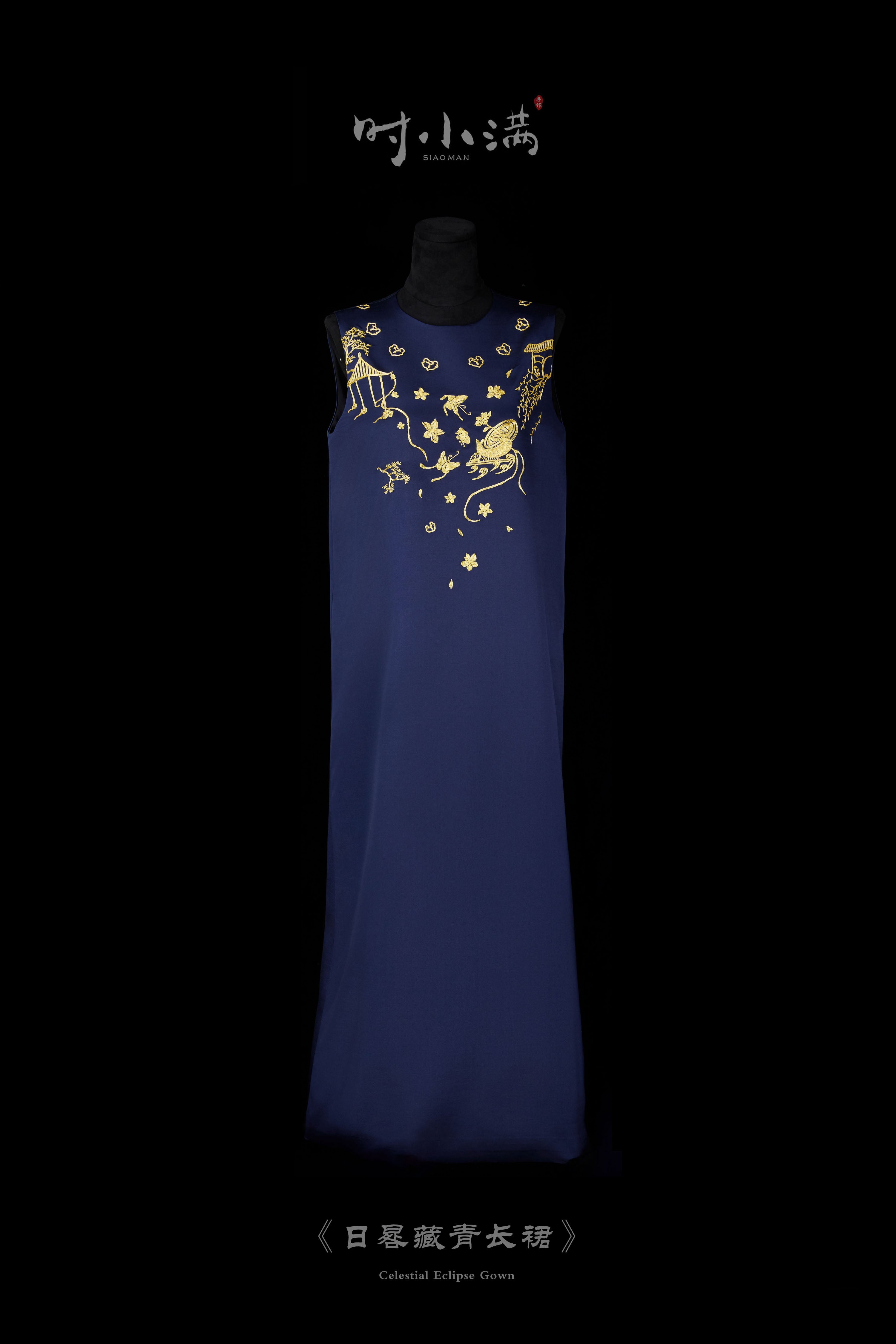A navy blue maxi gown with gold botanical embroidery on the chest, displayed against a black background.
