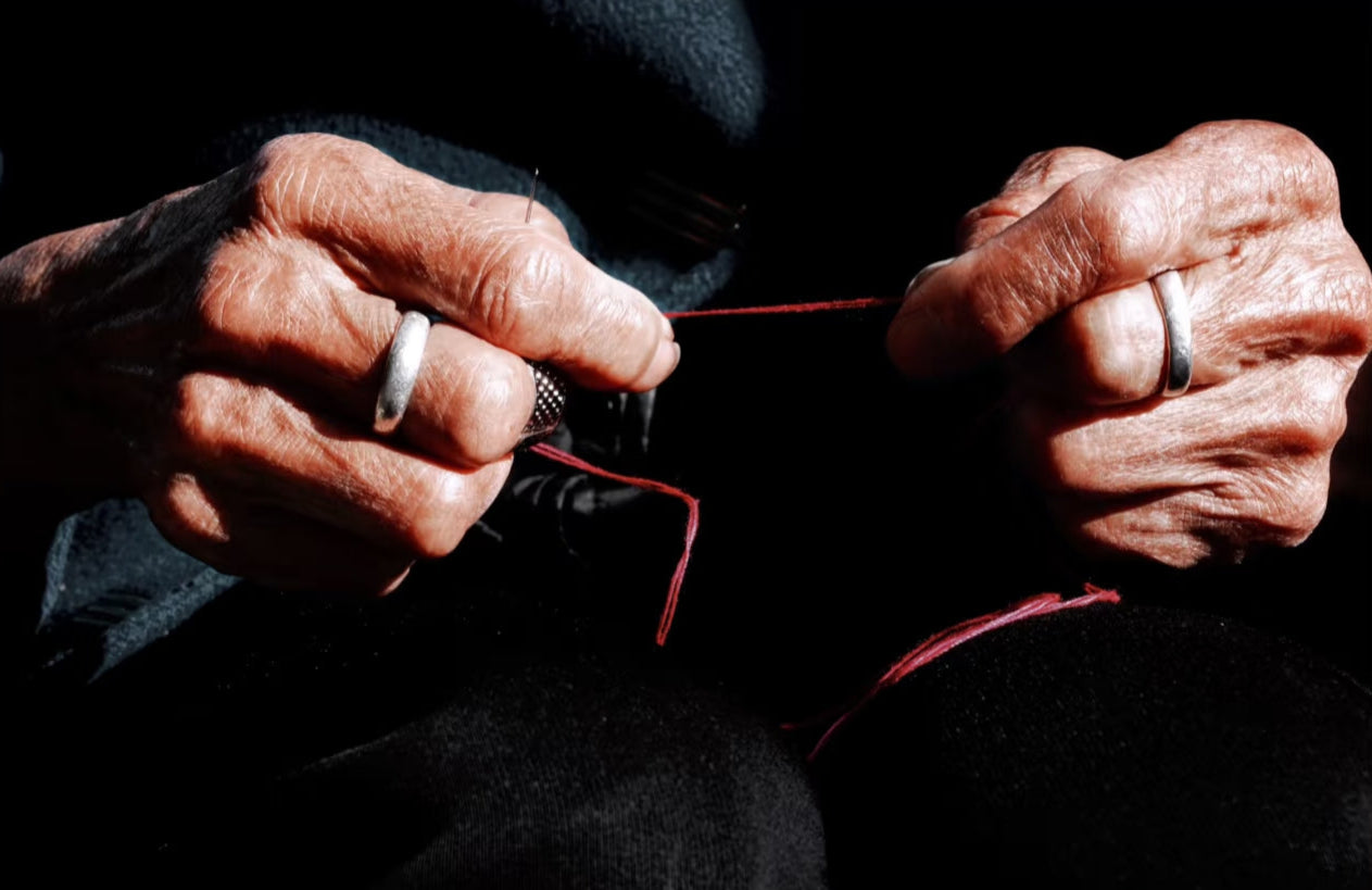 Close-up of hands with rings holding a thread against a dark background